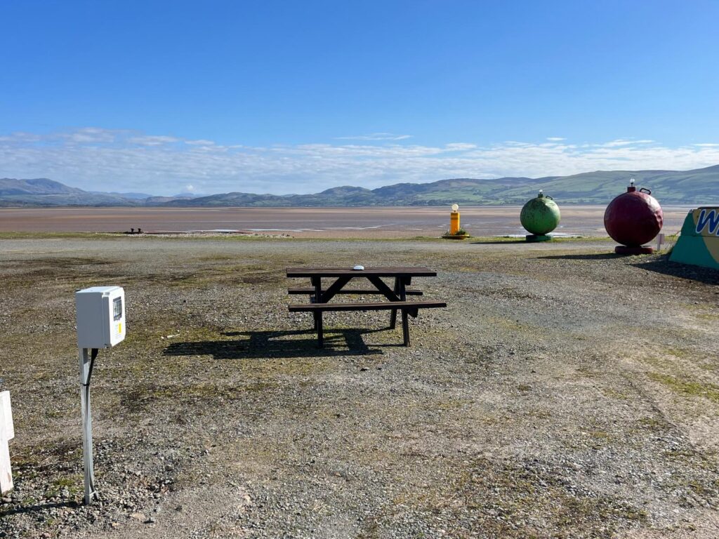 Picnic bench overlooking a coastal touring site with mountain views, open skies and electric hook-up facilities.